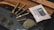 Several rolled cigars or blunts are placed on a wooden surface next to a humidity control packet. There is a display of scattered dried herbs or leaves.