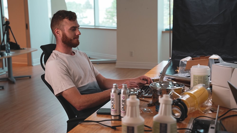 a man sitting at a desk with a computer and a group of bottles