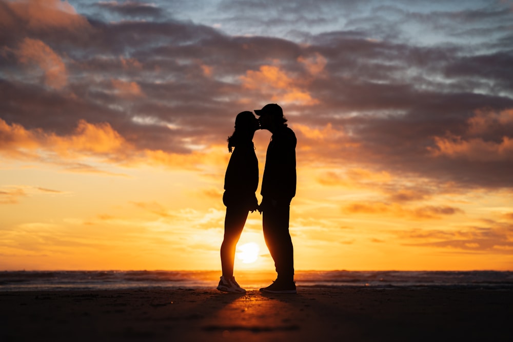 a man and woman kissing on a beach at sunset