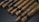 A collection of neatly arranged cigars lies on a dark surface. Each cigar is wrapped in brown leaf with visible veins and features a black band around its center.