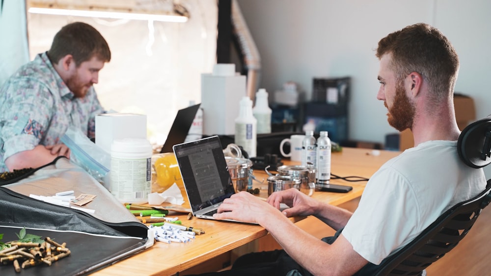 a man sitting at a desk with a laptop and another man sitting at a desk with a computer