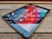 A tablet is placed on a wooden table, displaying a screen with various social media app icons such as Facebook, Instagram, LinkedIn, and Twitter. The reflection of lights above adds a dynamic visual effect to the screen.