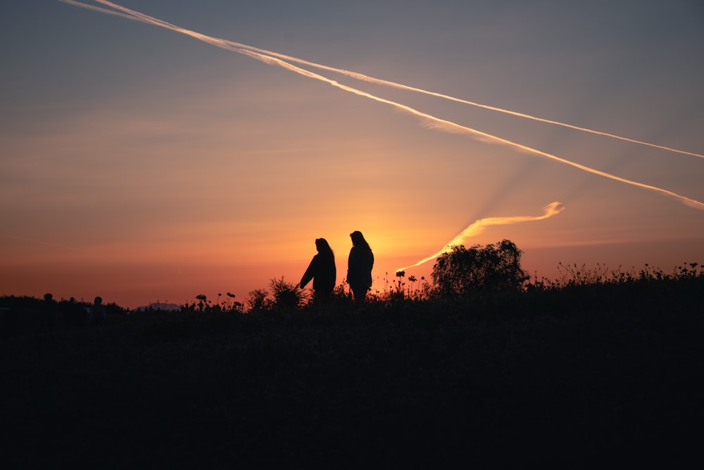 a couple of people standing in front of a sunset