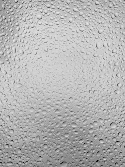 Close-up of crystal-clear water droplets on a polished surface reflecting light like diamonds.