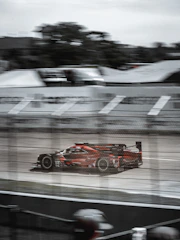 A dynamic racing car speeding on an endurance circuit under a bright sky.
