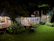 A cozy guesthouse with a welcoming porch surrounded by lush greenery at sunset.