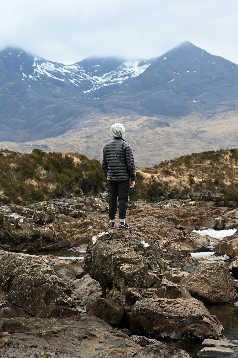 Una persona in piedi su una collina rocciosa che domina una catena montuosa innevata
