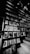 A black and white photograph featuring a wall filled with various framed magazine covers. The covers include images of people, abstract art, and typography. On the right, a staircase ascends alongside the display. The lighting creates dramatic shadows and highlights.