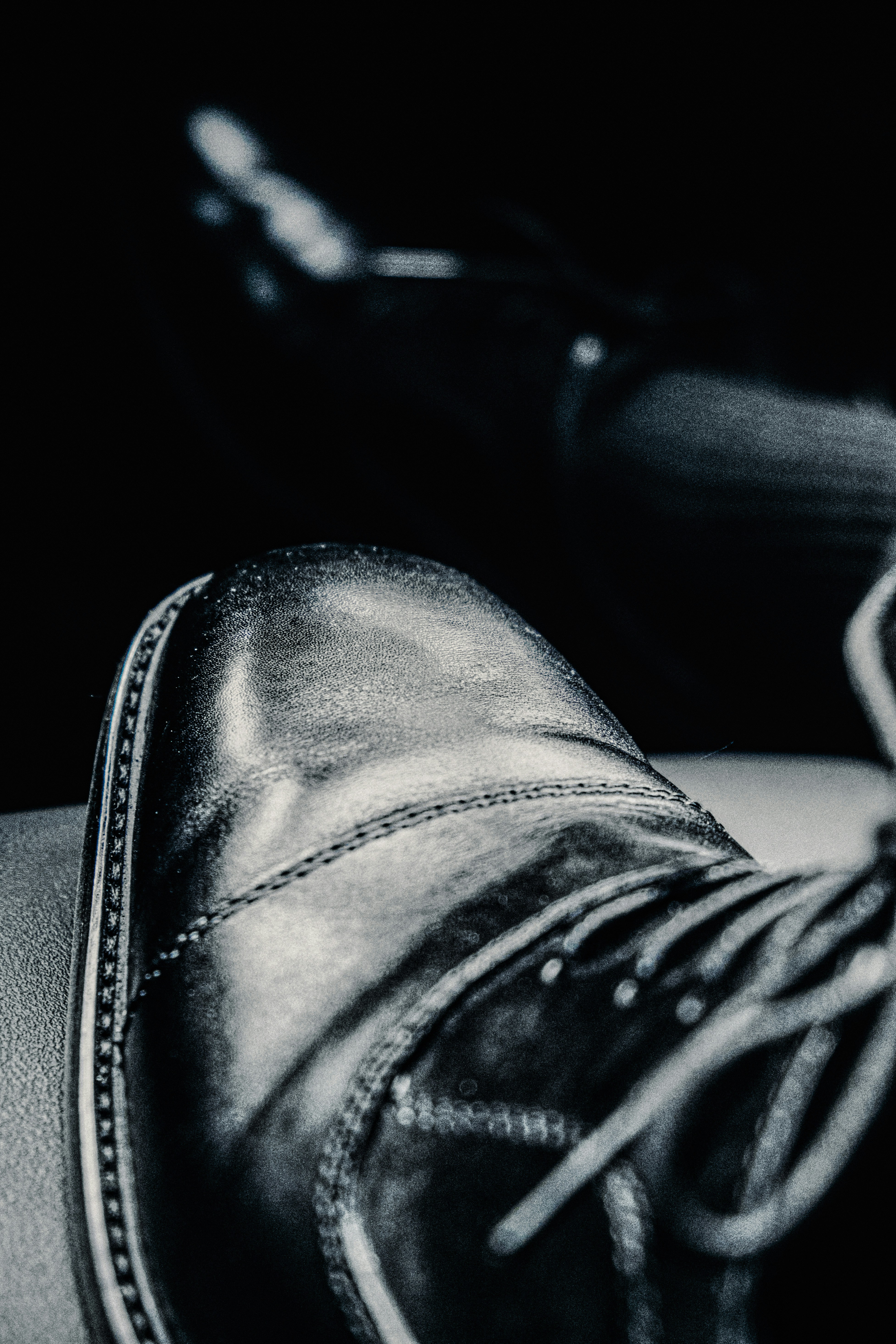 Close-up of polished leather shoes on dark background, dramatic side lighting, deep shadows, rich brown tones