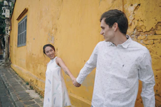 A candid moment of a couple walking hand in hand through a terracotta-colored street.