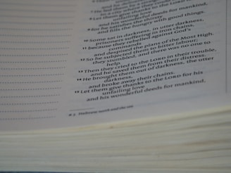 A close-up view of an open book with text focused on religious or biblical content. The visible lines of text are clear and legible, set on an off-white page with a noticeable thickness on the page edges.