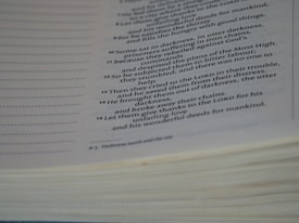 A close-up view of an open book with text focused on religious or biblical content. The visible lines of text are clear and legible, set on an off-white page with a noticeable thickness on the page edges.