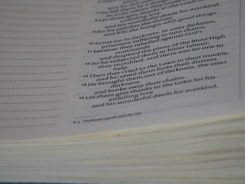 A close-up view of an open book with text focused on religious or biblical content. The visible lines of text are clear and legible, set on an off-white page with a noticeable thickness on the page edges.