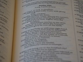A close-up view of an open book showing text from Psalm 108. The text is printed clearly and legibly, with the book slightly angled, revealing a soft focus on some of the words.