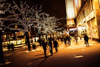 people walking on a street with trees with lights