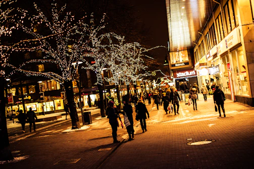 people walking on a street with trees with lights