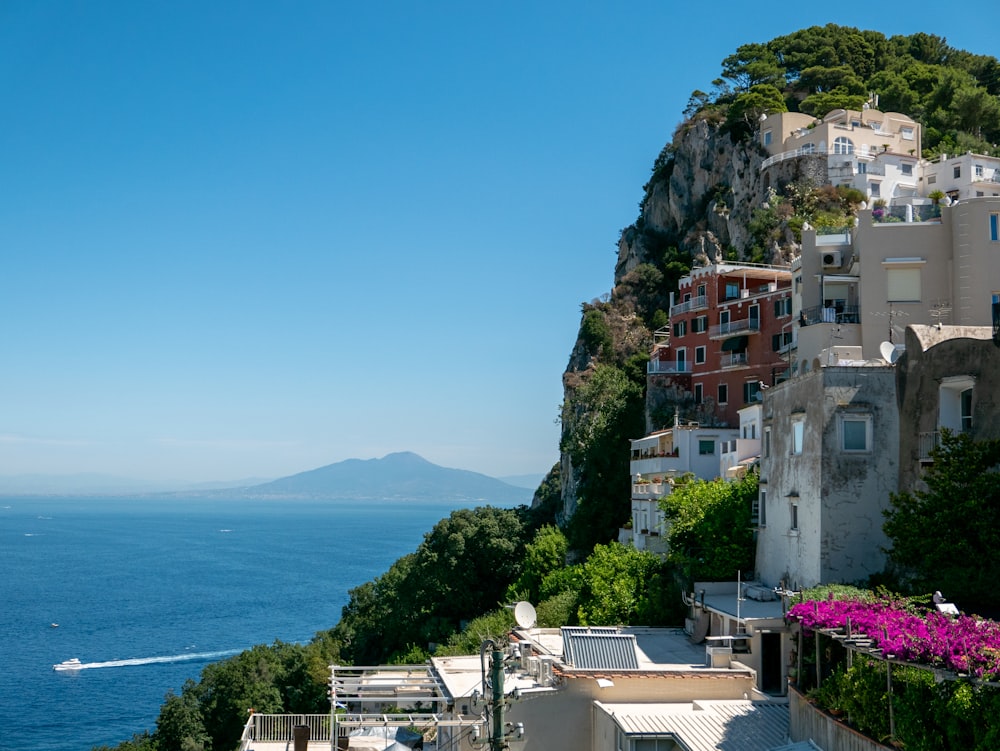 a hillside with buildings and trees by the water with Amalfi Coast in the background