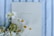 A spiritual journal with a beige cover lies on a fabric with blue and white stripes. Several white and yellow daisies are artfully arranged along the left side of the journal, adding a natural and calming touch.