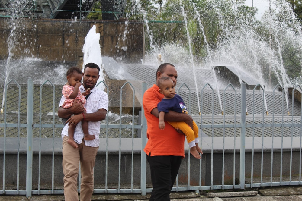 eine Person, die ein Baby hält und vor einem Brunnen steht