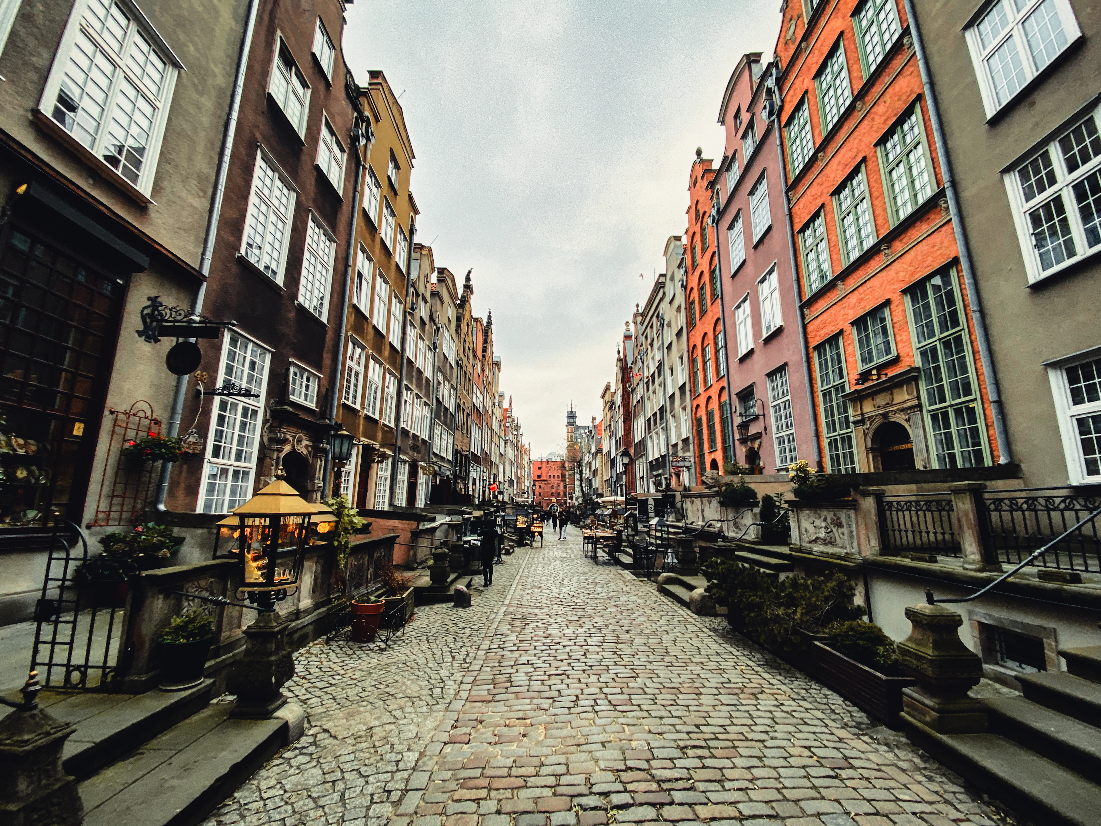Mariacka Street in Gdansk seen along its cobbles, the raised stone terraces and carved balustrades of the old merchant houses running away on both sides beneath tall painted gables, with the Gothic gate at the far end.