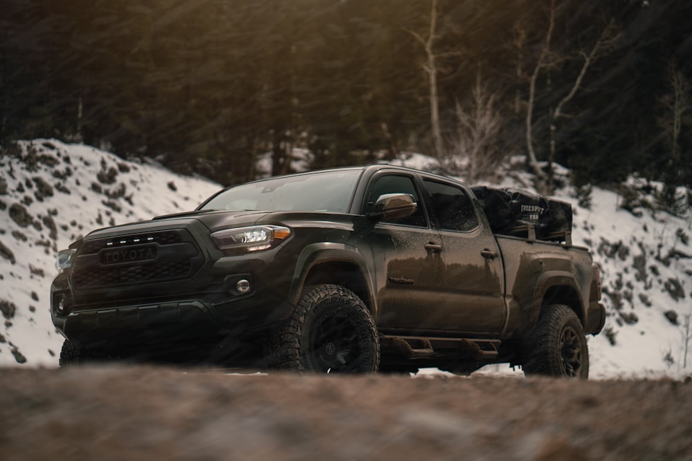 a black truck driving on a dirt road with snow on the side