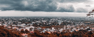 A panoramic view of a shadowy cityscape under a stormy sky, with neon signs barely visible.
