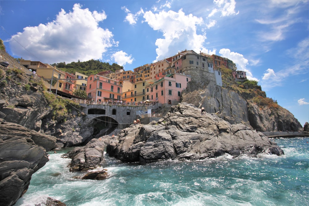a group of buildings on a rocky cliff over water with Cinque Terre in the background