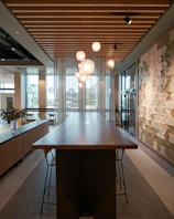Close-up of a rustic wooden table with metal legs, surrounded by industrial pendant lights hanging from a concrete ceiling.