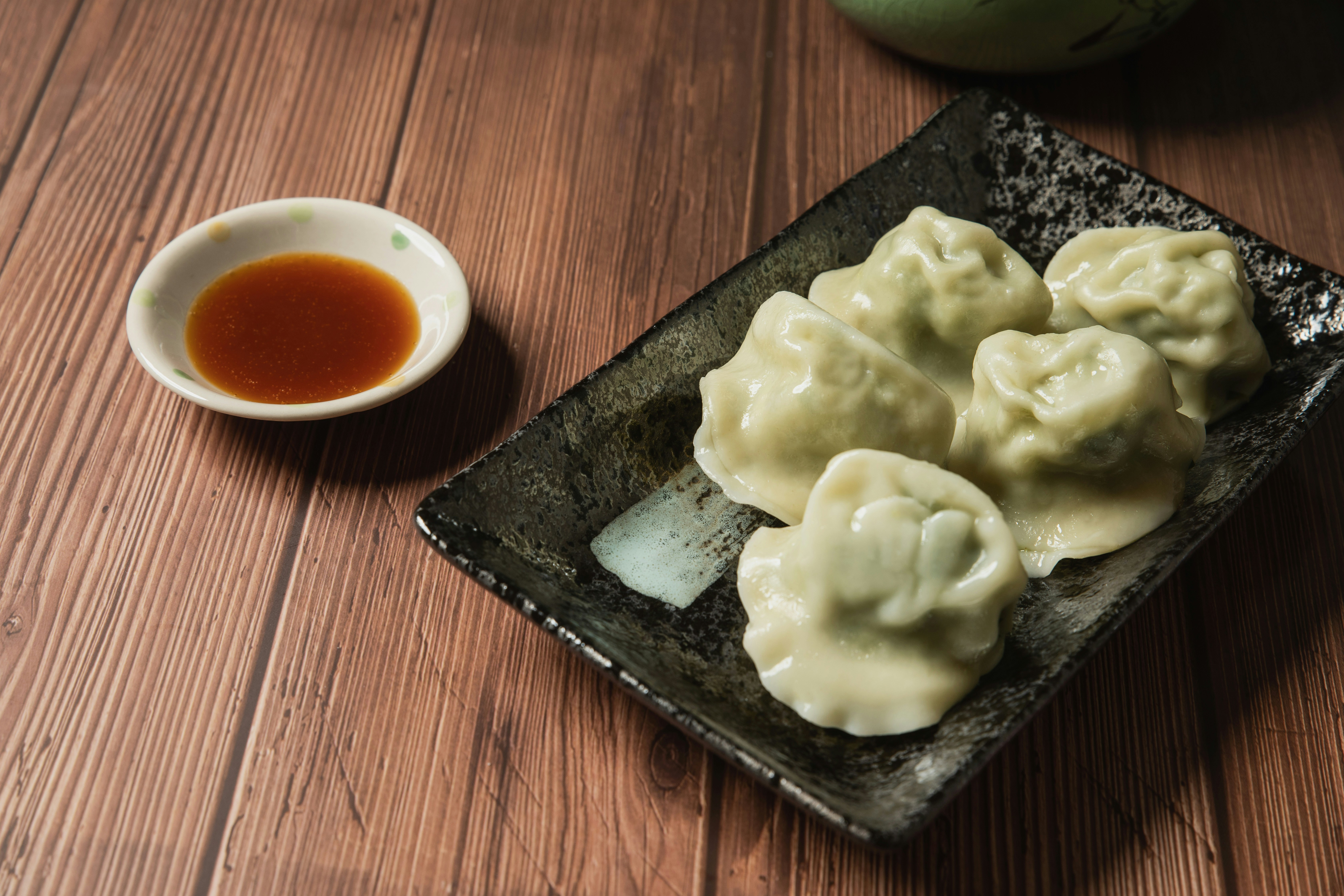 Green-tinted dumplings on a black plate with sauce