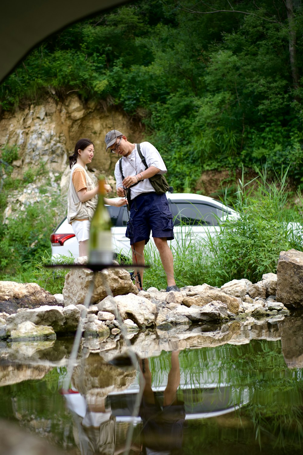 a man and woman standing on rocks by a pond