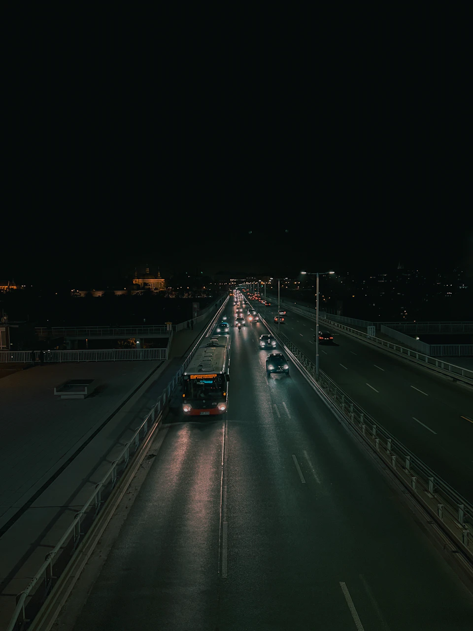 Dark highway stretches into darkness under string of streetlights at night with vehicles