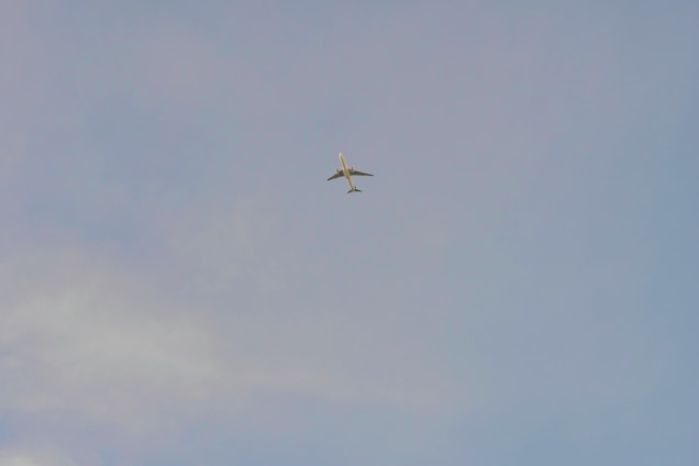 A sleek modern airplane flying above the clouds with a clear blue sky background.