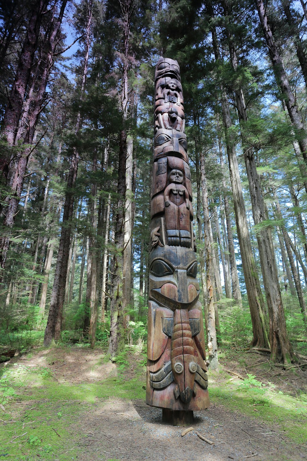 una scultura in legno di una persona con un volto su di esso in una foresta