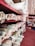 Multiple shelves are filled with rolled up fabric in various patterns and colors. The shelves are organized and display a variety of textures and designs suitable for upholstery or sewing projects. The floor is a deep red color, and some fabrics feature floral and geometric patterns.