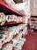Multiple shelves are filled with rolled up fabric in various patterns and colors. The shelves are organized and display a variety of textures and designs suitable for upholstery or sewing projects. The floor is a deep red color, and some fabrics feature floral and geometric patterns.