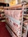 A display of various rolls of fabric on a rack, with patterns ranging from a world map to geometric and floral designs. A yellow sign above reads 'TELA RESINADA 6.50€ 1.40 ANCHO'. The setting appears to be a fabric store with shelves filled with different types of fabric.