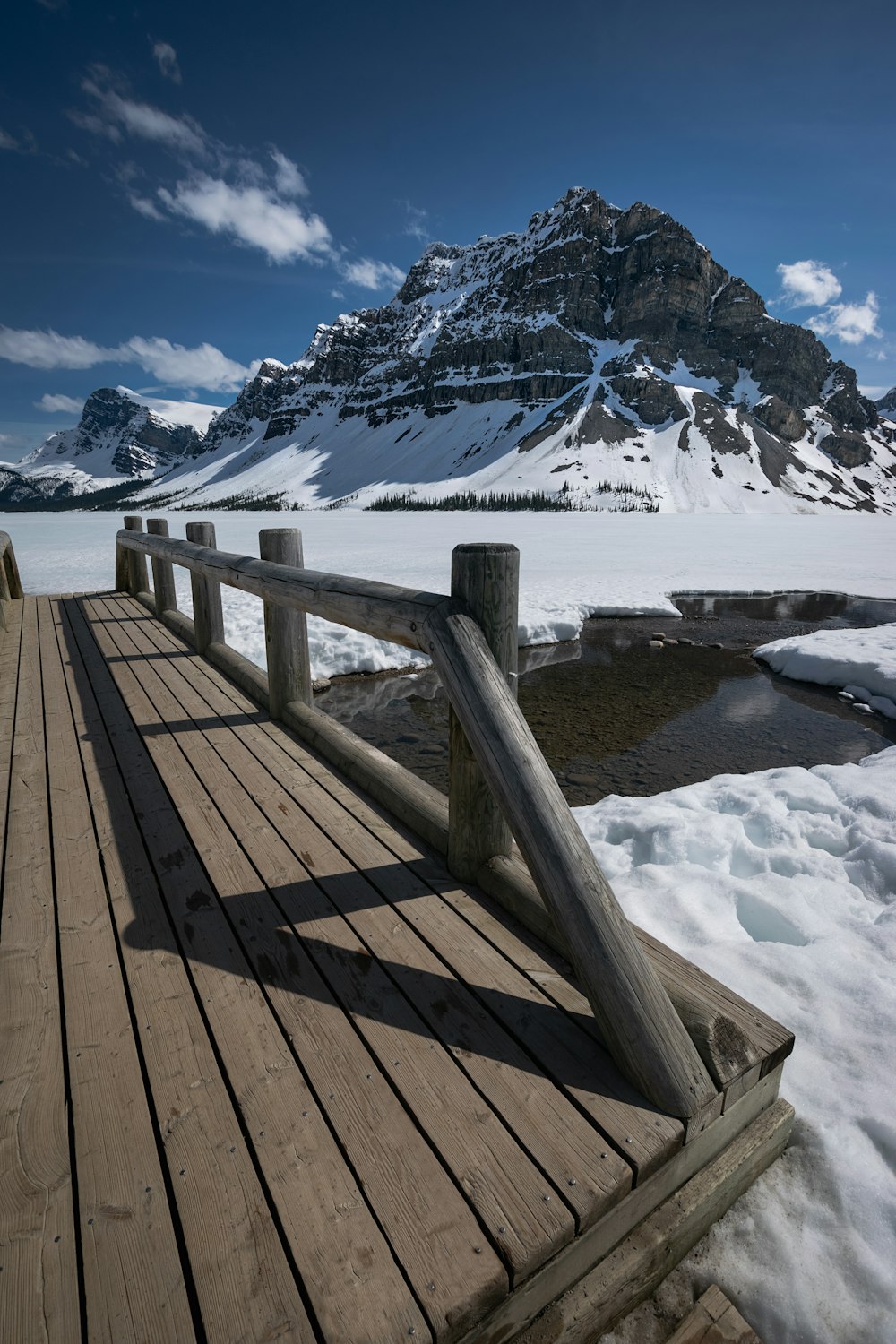 a wooden bridge over water with snow covered mountains in the background