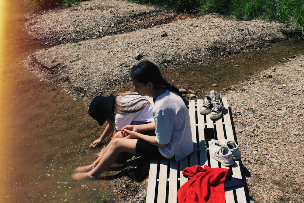 a couple of women sitting on a bench by a river