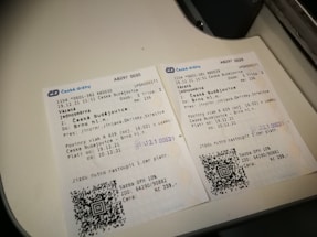 Two Czech train tickets are placed on a white surface. They contain details like departure and destination locations, travel dates, train numbers, and QR codes. Both tickets are for a journey from České Budějovice to Brno hl.n. The background suggests they are on a flat surface or countertop.