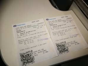 Two Czech train tickets are placed on a white surface. They contain details like departure and destination locations, travel dates, train numbers, and QR codes. Both tickets are for a journey from České Budějovice to Brno hl.n. The background suggests they are on a flat surface or countertop.