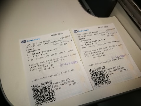 Two Czech train tickets are placed on a white surface. They contain details like departure and destination locations, travel dates, train numbers, and QR codes. Both tickets are for a journey from Česk&eacute; Budějovice to Brno hl.n. The background suggests they are on a flat surface or countertop.