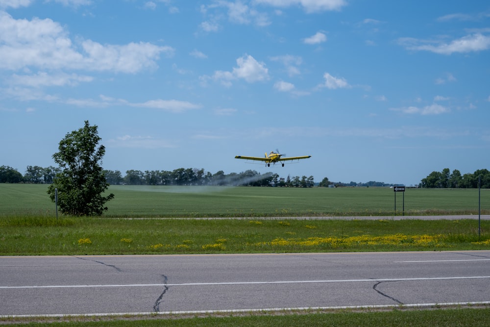 a yellow plane flying over a field