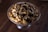 A glass bowl is filled with popcorn drizzled with rich chocolate and caramel. The popcorn appears glossy and decadent, sitting on a dark wooden surface which adds contrast to the presentation.