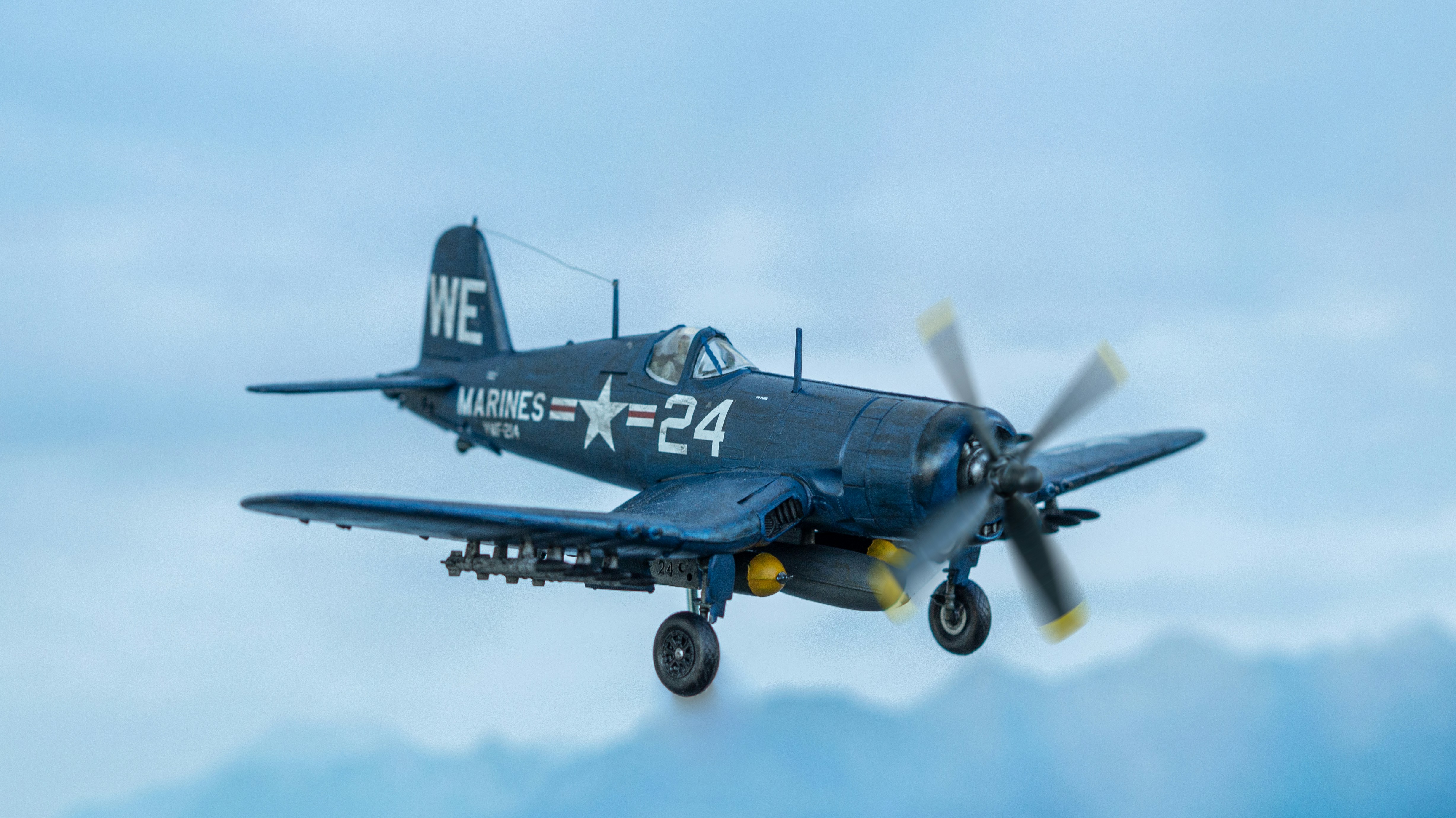 a plane flying in the sky, Diorama of a F4U Corsair scale model flying over the sea.
