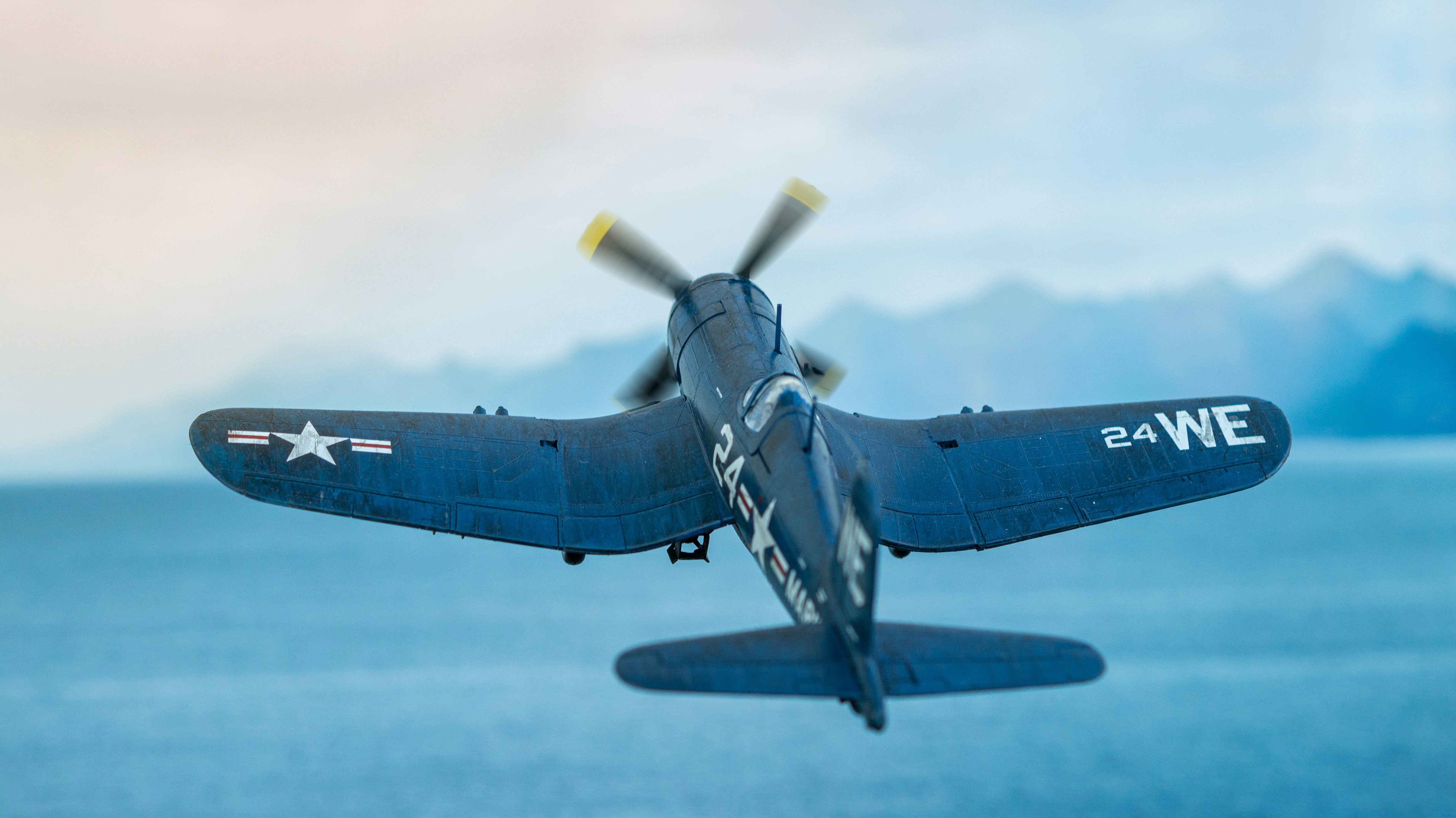 a military plane flying, Diorama of a F4U Corsair scale model flying over the sea.