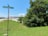 A street sign labeled 'Science.gov Way' stands in front of a grassy area beside a road. To the right, there is a large tree with dense green foliage. In the background, an industrial-looking building with a metal roof is visible beneath a clear blue sky.
