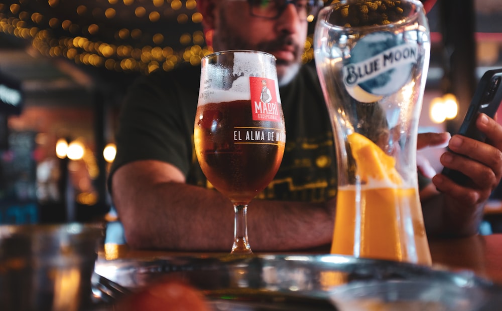 a person holding a cell phone next to a couple of glasses of beer