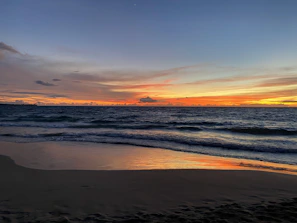 Golden sunset over a serene beach with gentle waves under a deep blue sky.