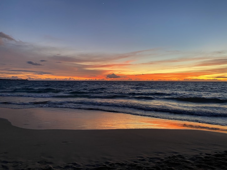 A vibrant sunset over a serene beach with gentle waves lapping the shore.