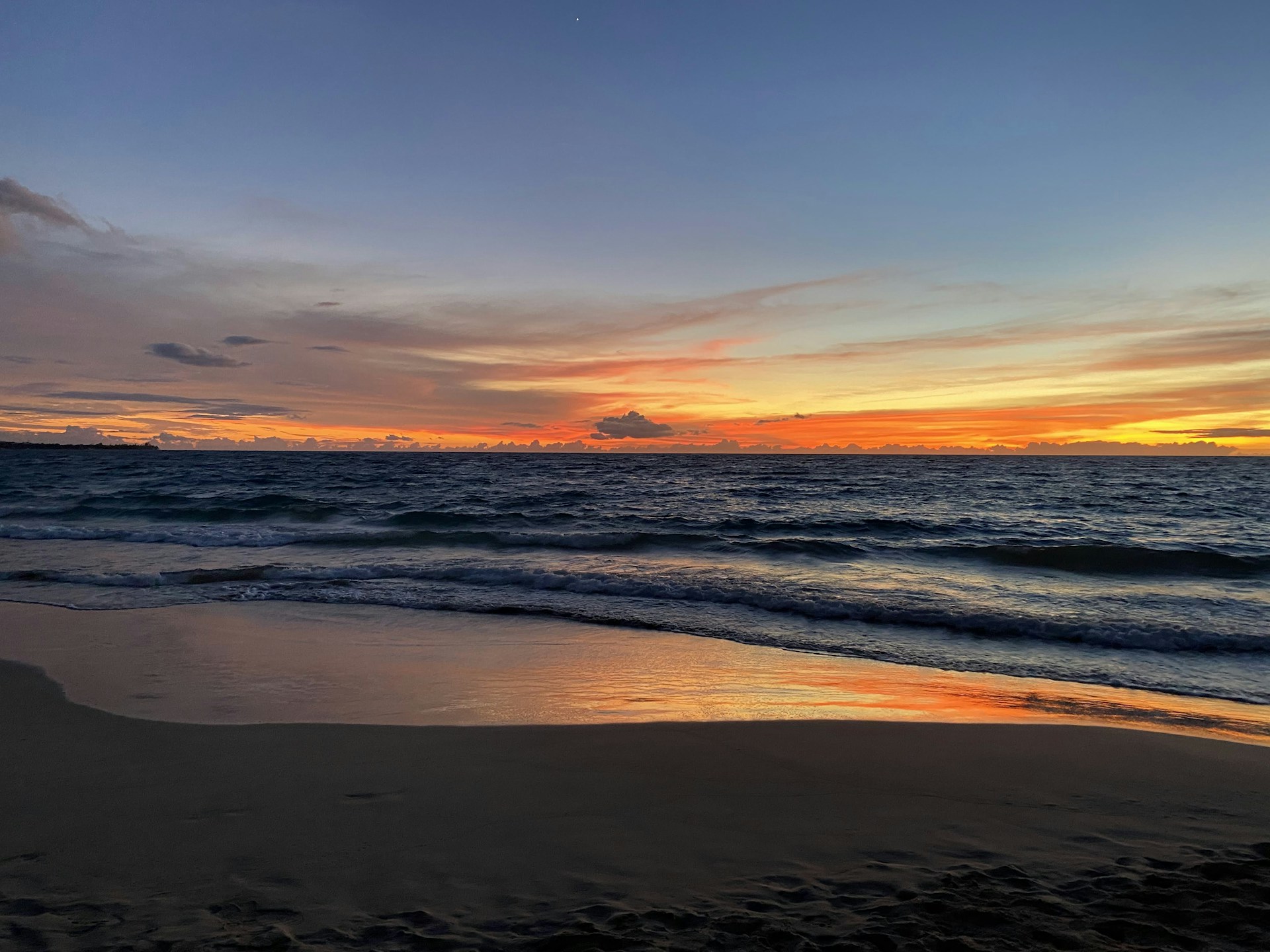 A vibrant sunset over a serene beach with gentle waves lapping the shore, capturing the calm of a perfect travel evening.